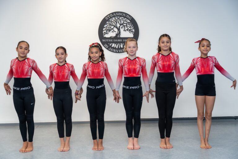 Six gymnastes en justaucorps rouge et noir alignées devant le logo de l’établissement.