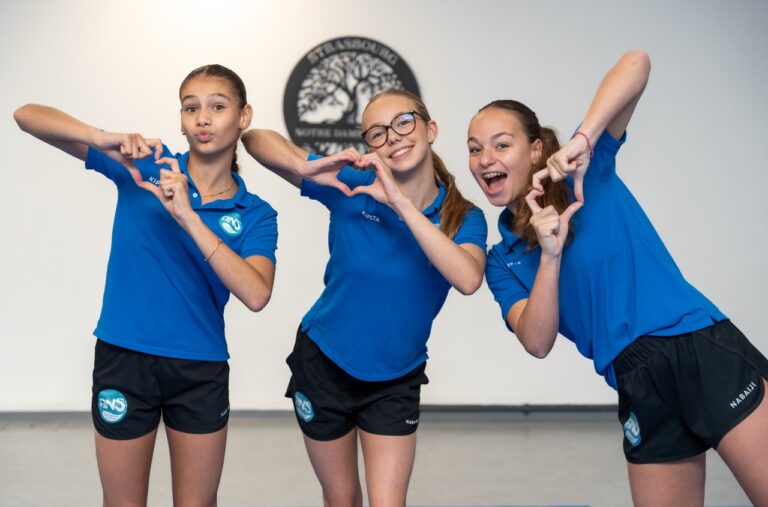 Trois élèves en polo du Ballet Nautique de Strasbourg forment des cœurs avec leurs mains.