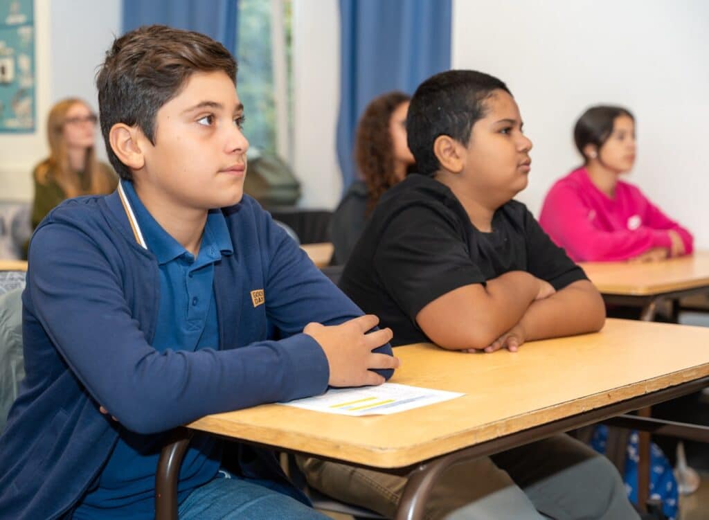 Des élèves assis à leurs tables suivent le cours dans une salle de classe.