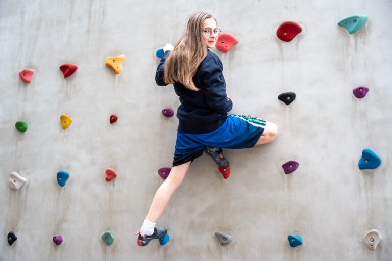 Une élève grimpe sur un mur d’escalade aux prises colorées.