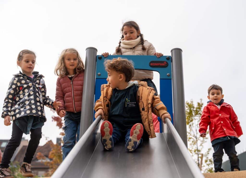 Un enfant descend le toboggan de la cour, une camarade attendant son tour en haut.
