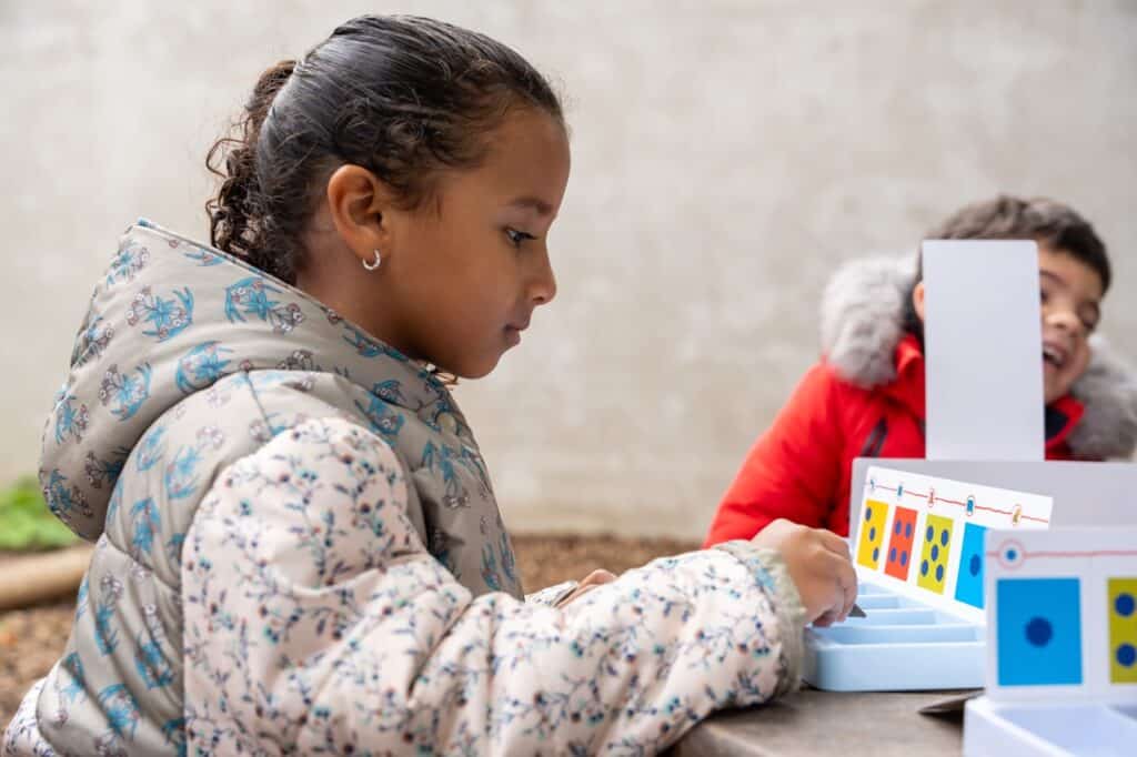 Deux élèves manipulent un jeu éducatif installé sur une table, dehors.